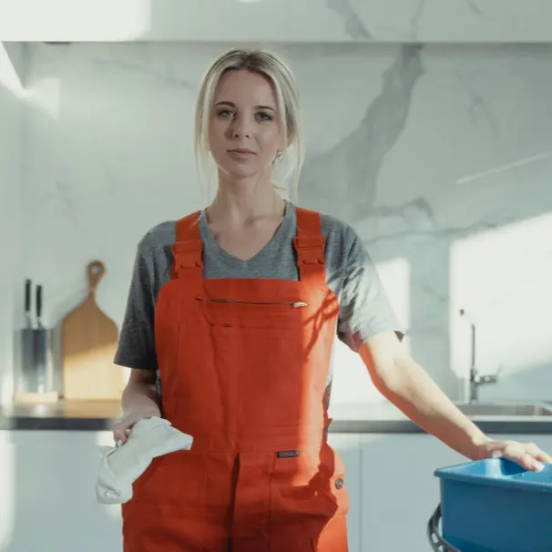 Young woman in orange apron cleaning kitchen with cloth.