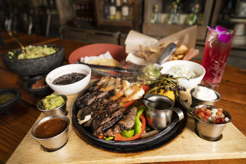 A sizzling platter of grilled meat with sides and sauces in a cozy restaurant.