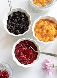 Three bowls of different colorful fruit jams with a spoon.