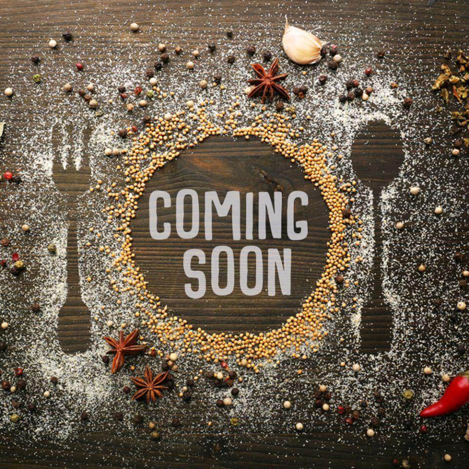 Spices and utensils arranged around a 'Coming Soon' sign on a textured surface.