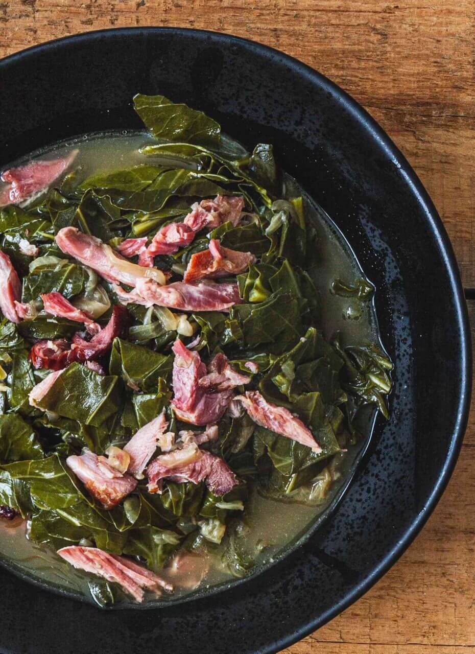 Collard greens with sliced bacon served in a black bowl.