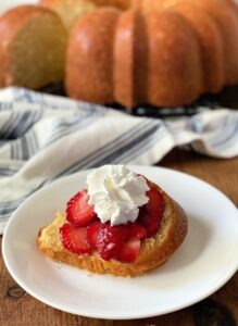 A biscuit topped with sliced strawberries and whipped cream on a white plate.