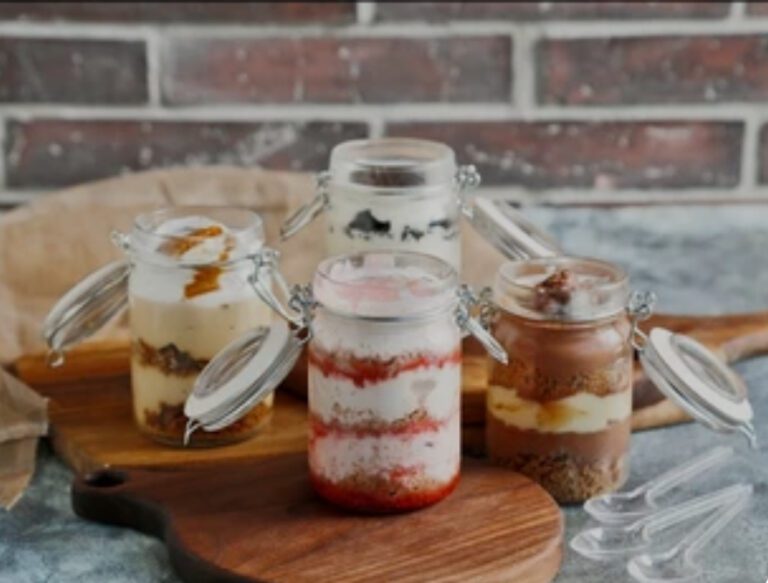 Four layered dessert jars with varied flavors on a wooden board.
