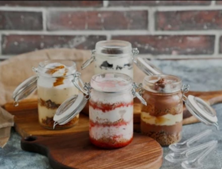 Four layered dessert jars with varied flavors on a wooden board.